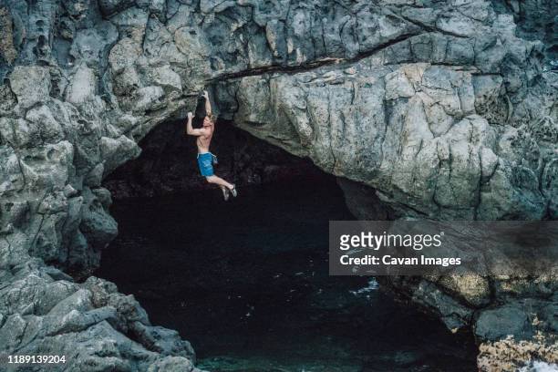 man climbing above the ocean in a volcanic cave - bouldering - fotografias e filmes do acervo