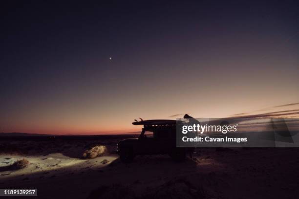 girl climbing to the roof of the 4x4 during the blue hour - wild overland stockfoto's en -beelden