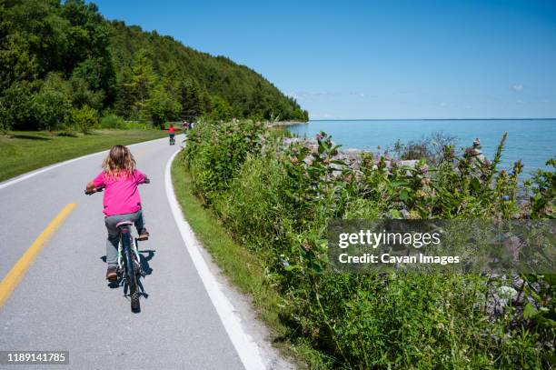 child riding bicycle on lake shore road on mackinac island - mackinac island stock-fotos und bilder
