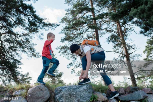 mother tying up her shoelace whilst walking with her son - boy tying shoes stock-fotos und bilder