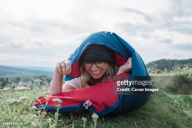 portrait of a woman laughing in a sleeping bag whilst camping on hill - business milestones stock pictures, royalty-free photos & images