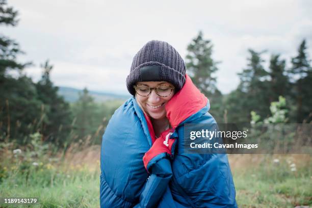 portrait of a woman smiling wrapped in a sleeping bag wild camping - amazing moment in the nature stock-fotos und bilder