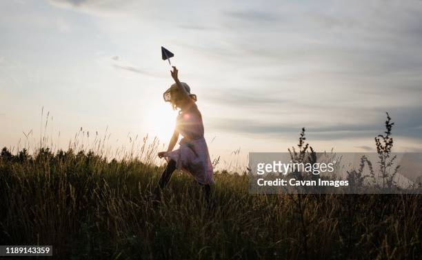 girl chasing a paper aeroplane in a meadow at sunset - paper airplane stock-fotos und bilder