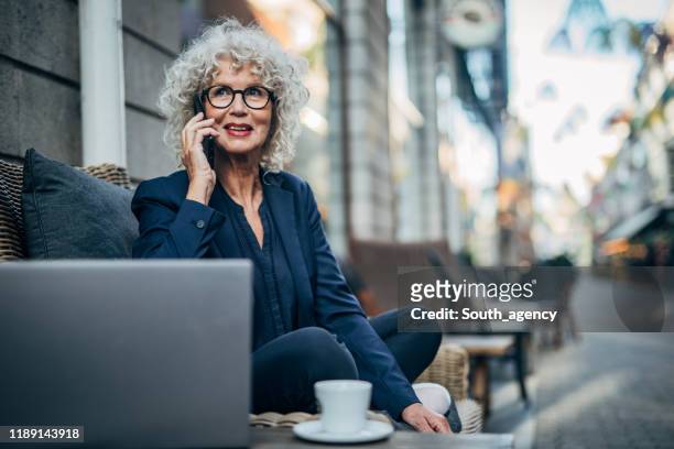 senior lady talking on mobile outdoors in cafe - city life stock pictures, royalty-free photos & images