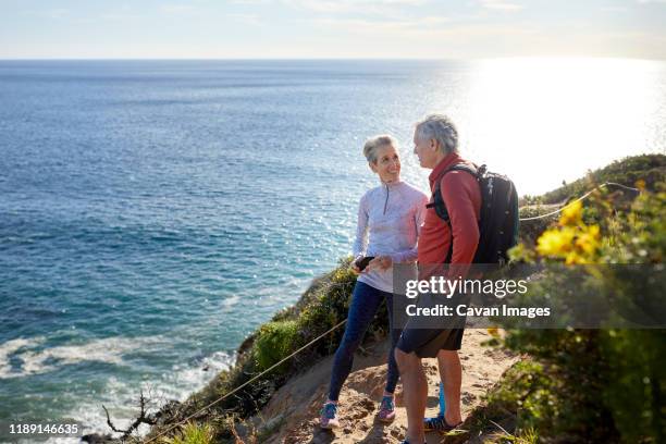 full length smiling senior couple talking while standing on cliff by sea during sunny day - guy with phone full image ストックフォトと画像