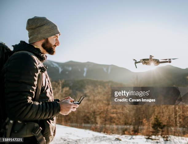 a man with a beard flies a drone in the mountains in winter. - camera operator imagens e fotografias de stock