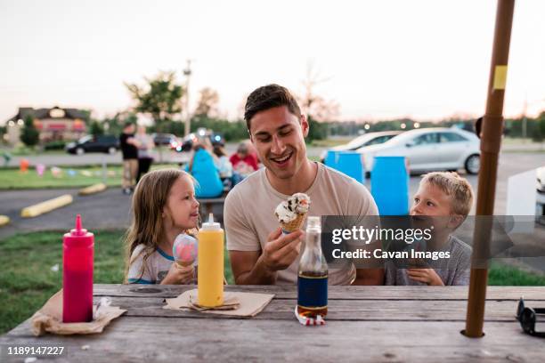 young man and children eat ice cream at picnic table on summer evening - uncle fotografías e imágenes de stock