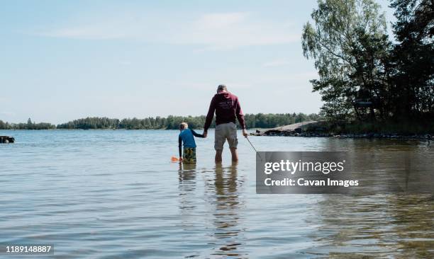 father holding his son's hand whilst fishing with a net in the sea - moment of silence stock-fotos und bilder