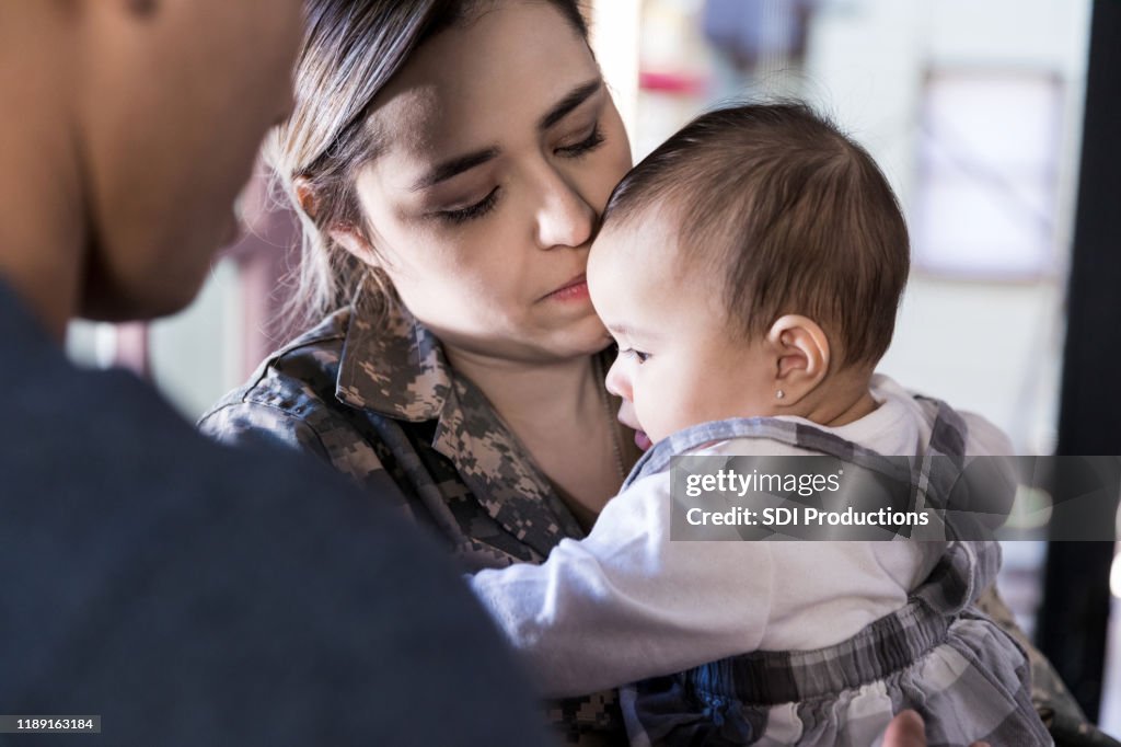 Close up photo of soldier mother holding baby; husband watches