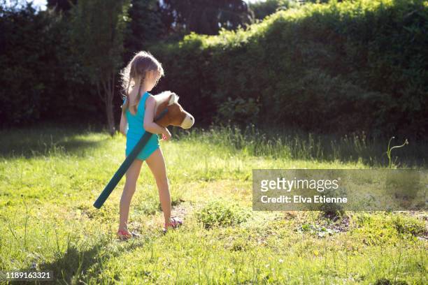 girl walking through summer grass in a back yard, carrying a hobby horse - hobby horse stock pictures, royalty-free photos & images