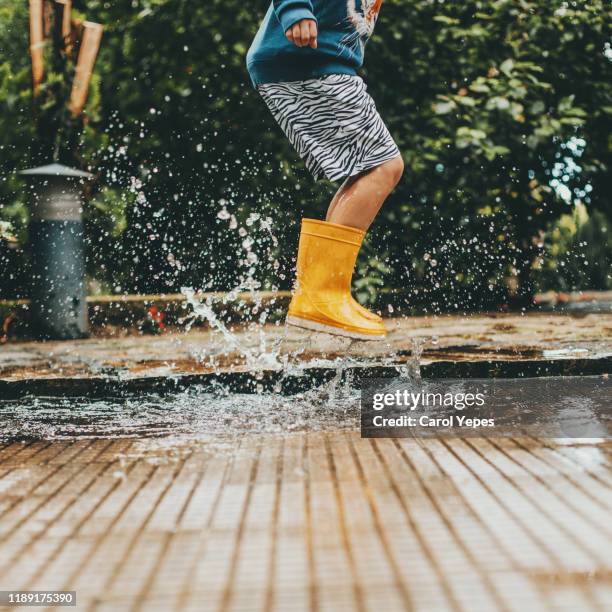 boy playing puddles - rubberlaars stockfoto's en -beelden