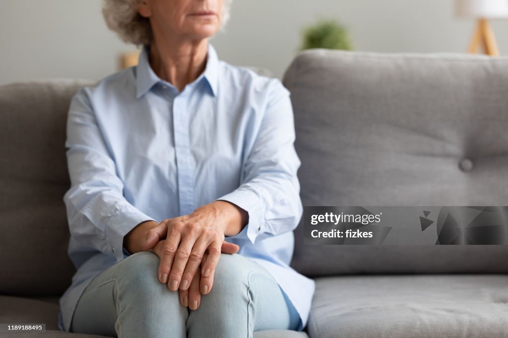 Unhappy depressed senior woman sit alone on sofa, closeup view