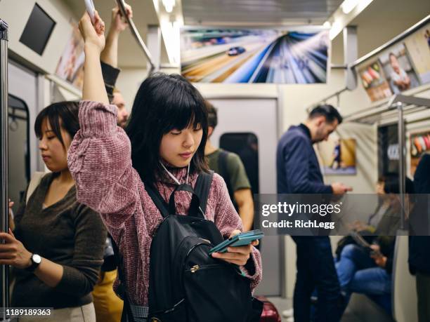jonge vrouw op een drukke japanse metro trein - crowded train station smartphone stockfoto's en -beelden