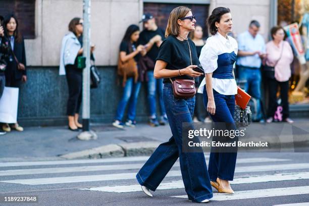 Guest wears sunglasses, necklaces, a black top with rolled-up short sleeves, a burgundy crossbody bag, navy blue denim full length flare pants, white...