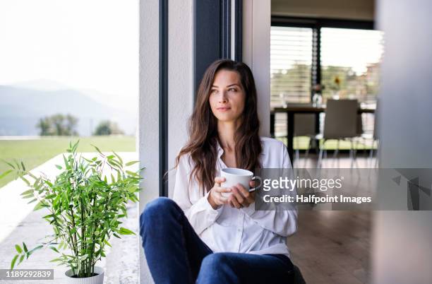 portrait of young woman with coffee sitting by patio door at home. - coffee on patio stock pictures, royalty-free photos & images