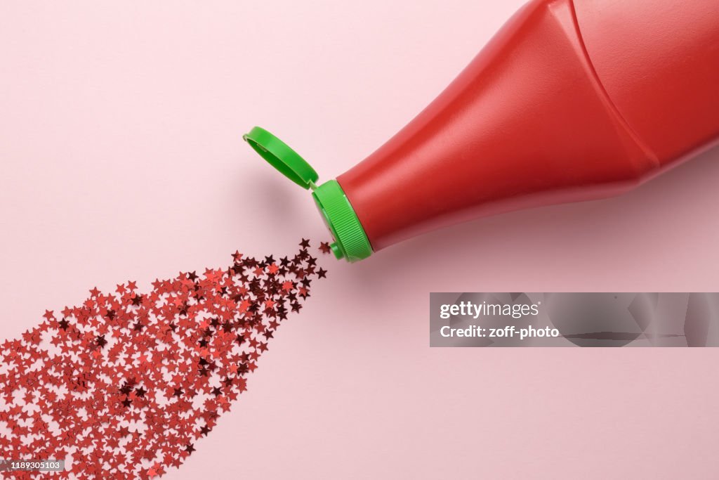 Flat lay of plastic ketchup bottle and red stars in form of tomato sauce on pastel pink background abstract.