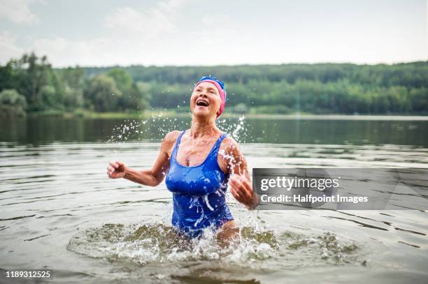 active senior woman standing in lake outdoors in nature, splashing water. - badkläder bildbanksfoton och bilder