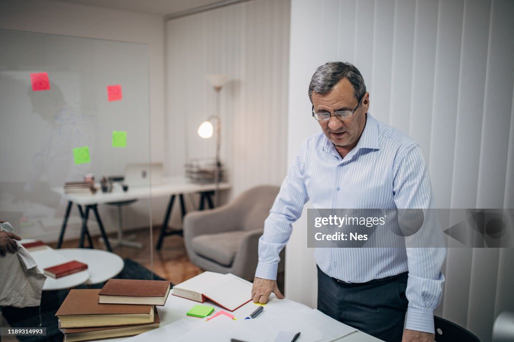 An old business man is standing at his desk
