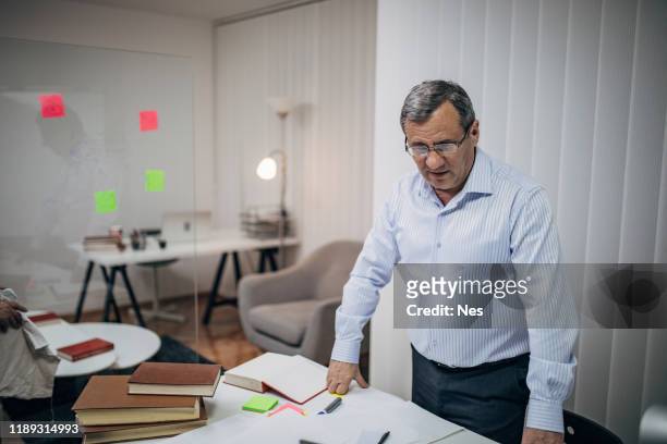an old business man is standing at his desk - funcionário público imagens e fotografias de stock