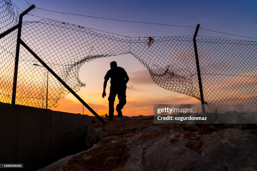 Refugee man running behind fence,