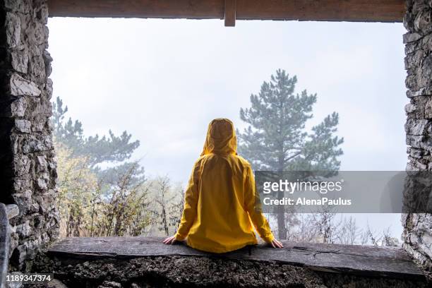 person in yellow rain coat sitting in a shelter in mountains hiding from the rain back view - storm outside window stock pictures, royalty-free photos & images