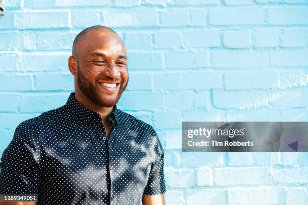 man smiling abasing blue wall - oberkörper happy sommersprossen stock-fotos und bilder