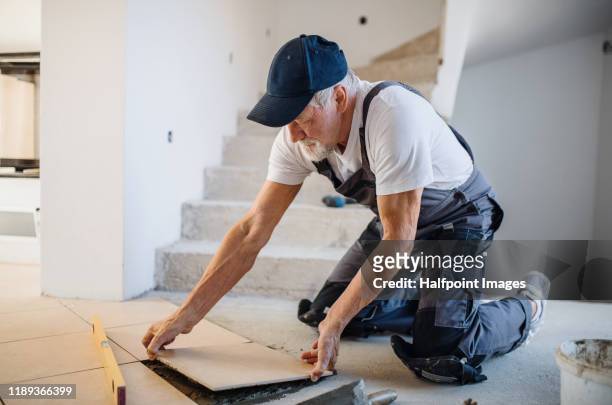 senior man laying tile floor in new home. - flooring installation stock pictures, royalty-free photos & images