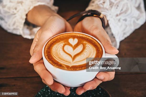 cropped shot of woman hands holding a cup of hot latte coffee in her hands. - kaffee becher stock-fotos und bilder