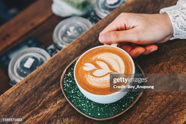 cropped shot view of woman hand touching a cup of hot latte coffee on the wooden table. - coffee heart fotografías e imágenes de stock