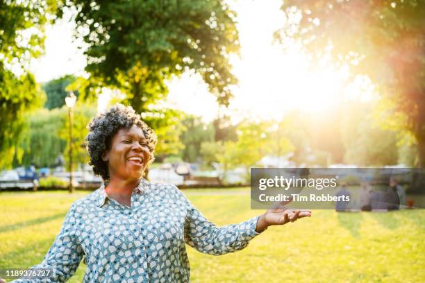 happy woman with arms out in park - images of fat black women stock-fotos und bilder