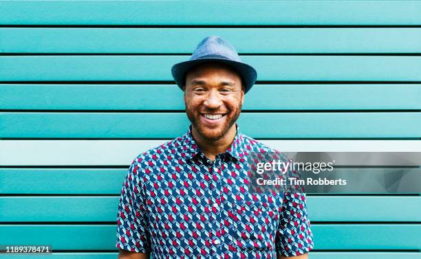 portrait of happy man against blue wall - black hat stockfoto's en -beelden