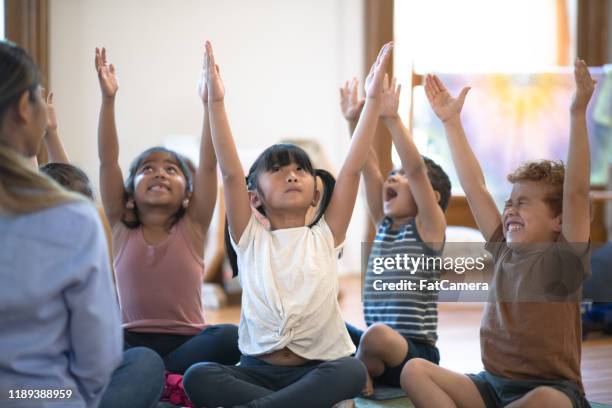 groupe multiethnique d'enfants assis sur un tapis avec leur photo stock d'enseignant - yoga rug photos et images de collection