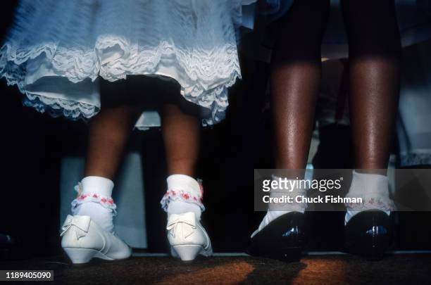 Close-up, from behind, of the feet and lower legs of a pair two young girls in the Gospel Tent during the New Orleans Jazz Festival, New Orleans,...