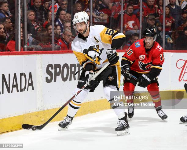 Kris Letang of the Pittsburgh Penguins players the puck as hes pursued by Derek Ryan of the Calgary Flames during an NHL game on December 17, 2019 at...