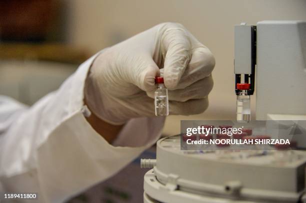In this photograph taken on November 12 a pharmacist holds a small flask as he examines seized samples of drugs to identify the substance in the...
