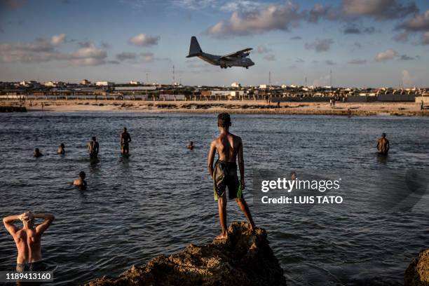 Soldiers enjoying a day off and Somali people look from the beach at a military plane landing within Mogadishu's airport base in Mogadishu, Somalia,...