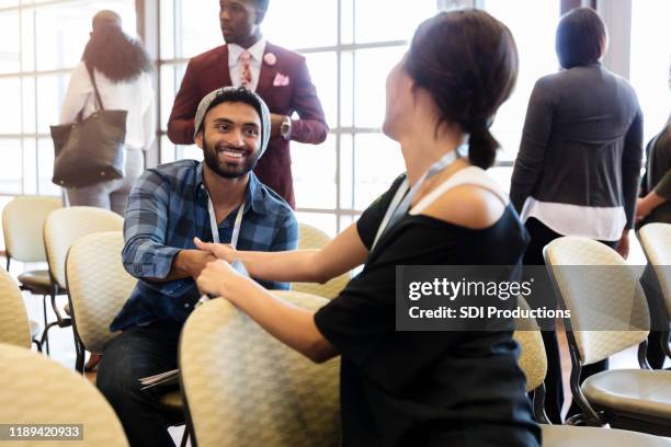 millennial man greets friend during expo - diverse town hall meeting stock pictures, royalty-free photos & images