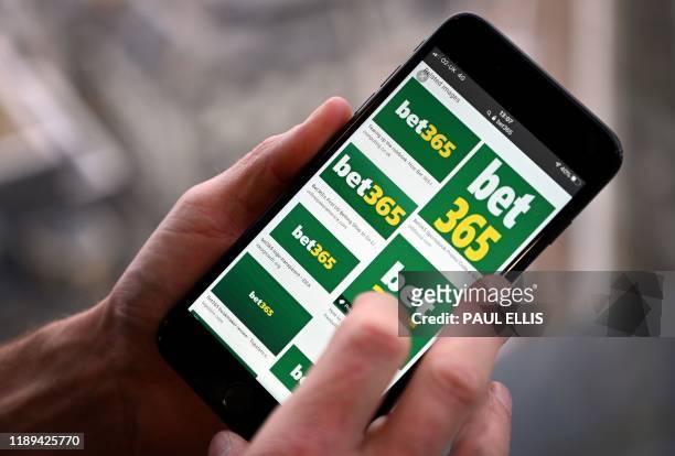Man poses for a photograph with the logo for online gambling website Bet365 displayed on a smartphone, in London on December 18, 2019. - Denise...