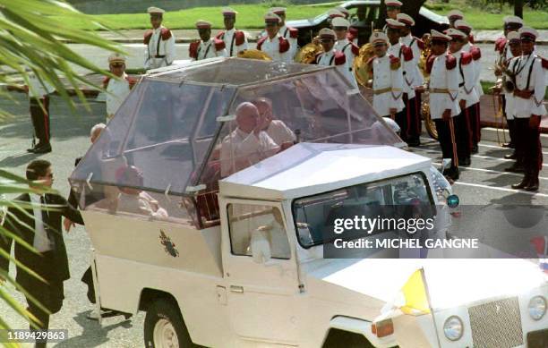 Pope John Paul II waves to people gathered outside the gates of the Presidential Palace in Santo Domingo 10 October, 1992 as he arrives to meet with...