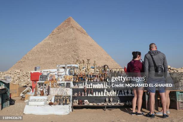 Tourists buy souvenirs at the Giza pyramids necropolis on the southwestern outskirts of the Egyptian capital Cairo on December 18 with the pyramid of...