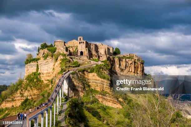 Civita di Bagnoregio, an old etruscan settlement, located on top of a volcanic tuff plateau, illuminated by the setting sun, dark thunderstorm clouds...