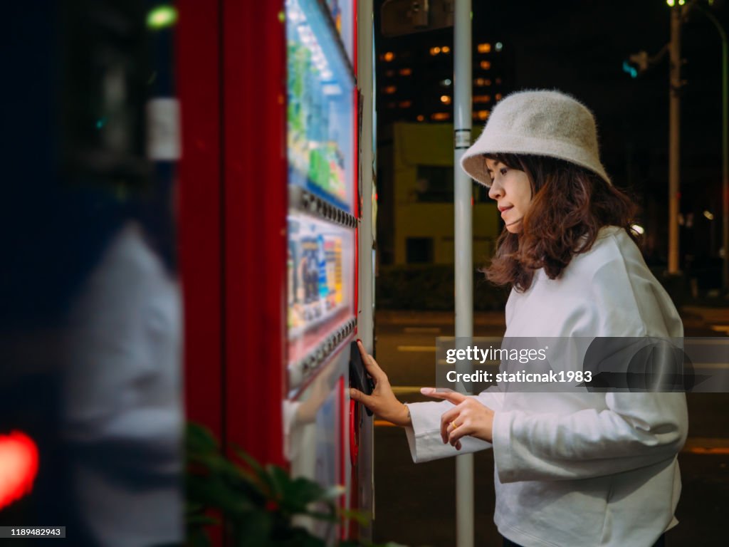 Donna asiatica che paga con lo smartphone al distributore automatico.