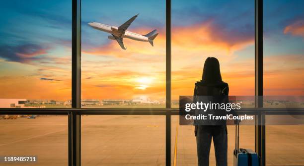 travel tourist standing with luggage watching sunset at airport window. woman looking at lounge looking at airplanes while waiting at boarding gate before departure. travel lifestyle. transport and travel concept - tabellone arrivi e partenze foto e immagini stock
