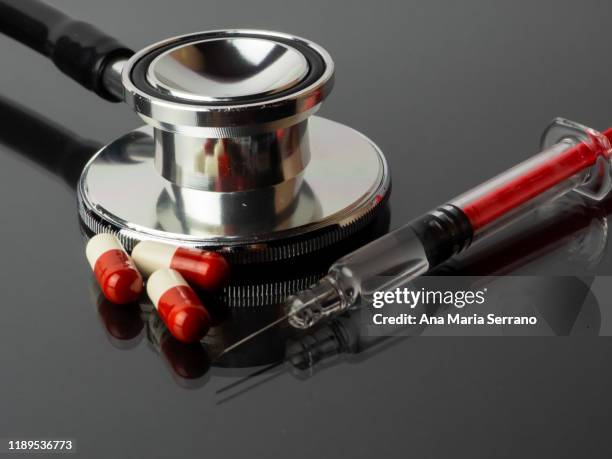 a syringe, stethoscope and several pills reflected on a gray background with mirror effect - heart pill ストックフォトと画像