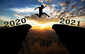 A young man jump between 2020 and 2021 years over the sun and through on the gap of hill  silhouette evening colorful sky.