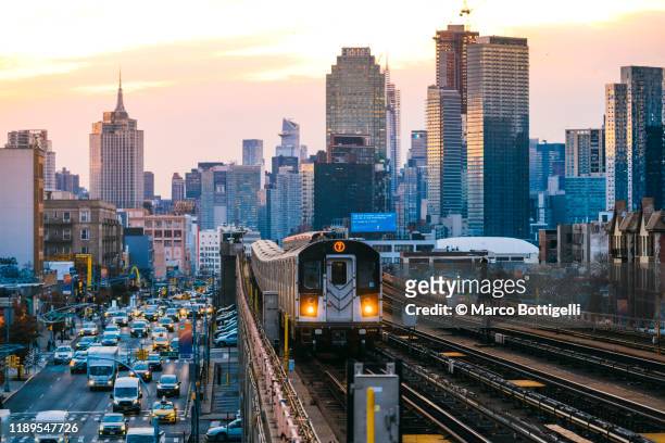 7 line subway train in queens with manhattan skyline, new york city - hauptverkehrszeit stock-fotos und bilder