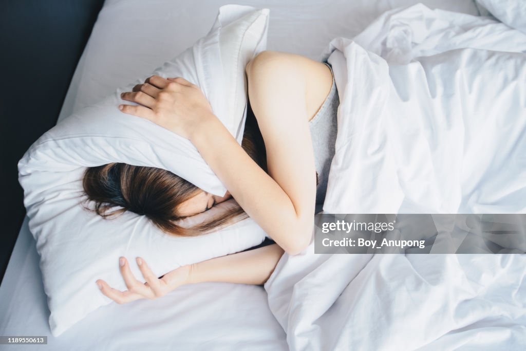 High angle view of young woman lying on bed and she hate to waking up in the early morning.