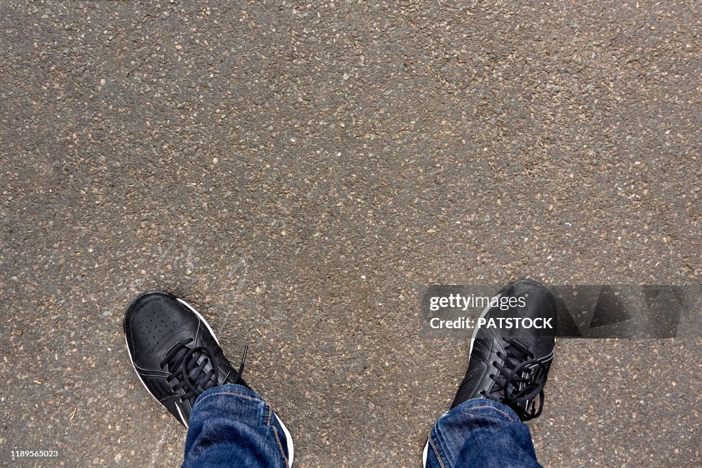 Low section of teenager standing on asphalt road