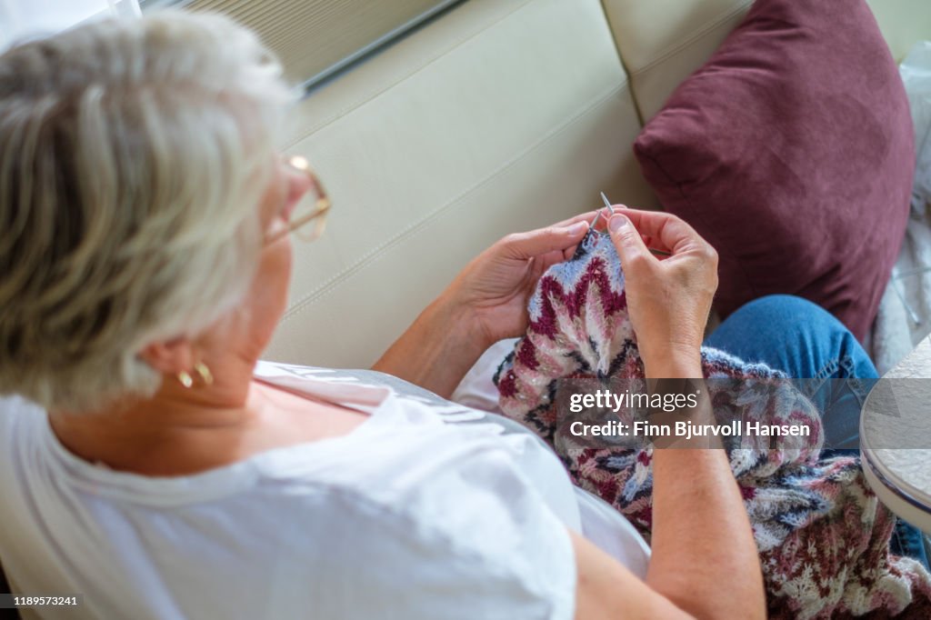 Woman sitting in the sofa knitting a scarf