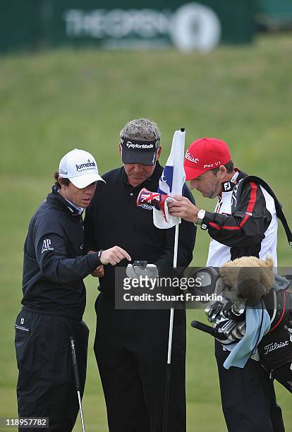 Rory McIlroy and Darren Clarke of Northern Ireland look at a mobile phone alongside caddie J.P. Fitzgerald during the final practice round during The...